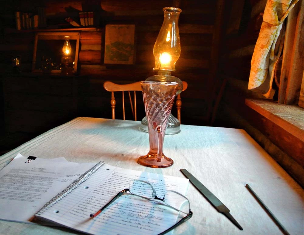 Image of a table, gas latern, and notebook on the dinning table inside the cabin.